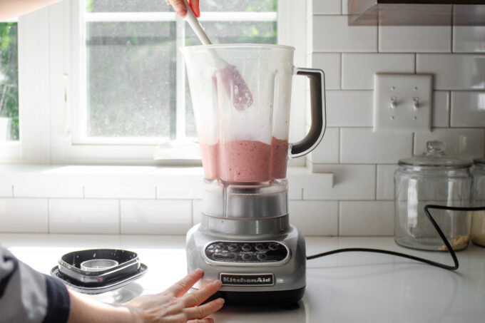 A strawberry milkshake made without ice cream on a white countertop with fresh strawberries to the side.