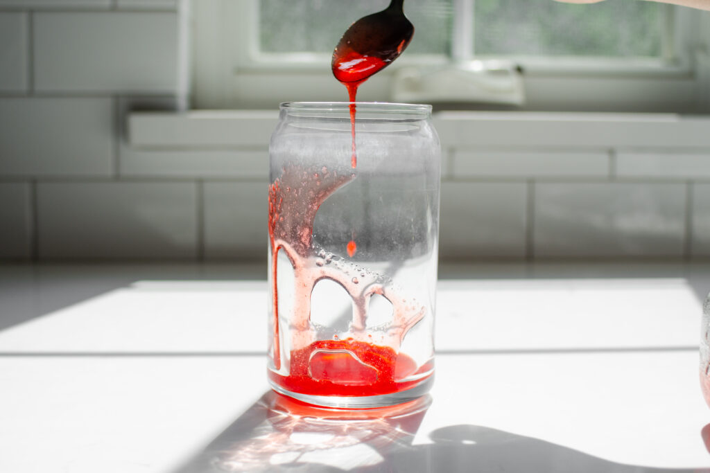 Pouring strawberry syrup into a glass.