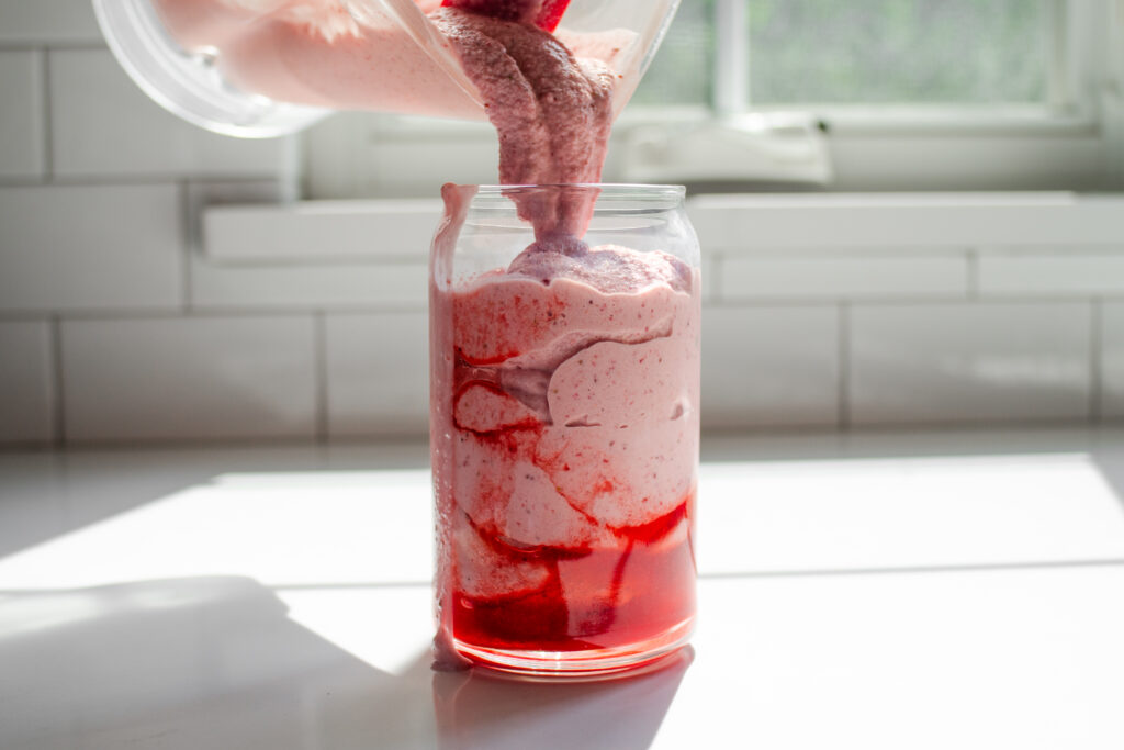 Pouring the strawberry milkshake into a serving glass.