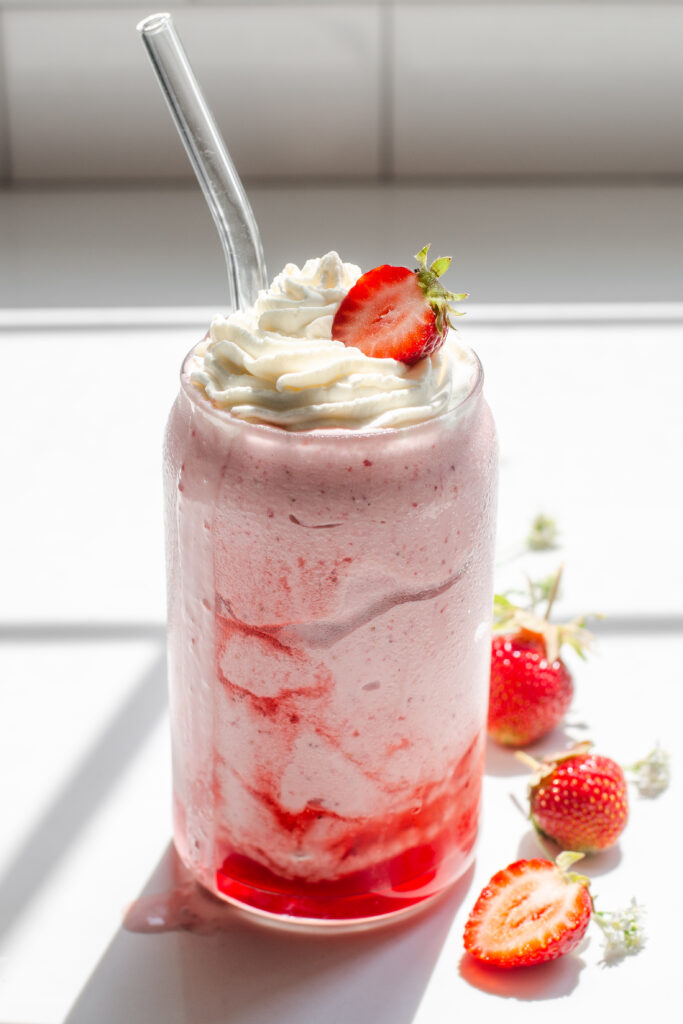 A strawberry milkshake on a white countertop with whipped cream and a strawberry on top.