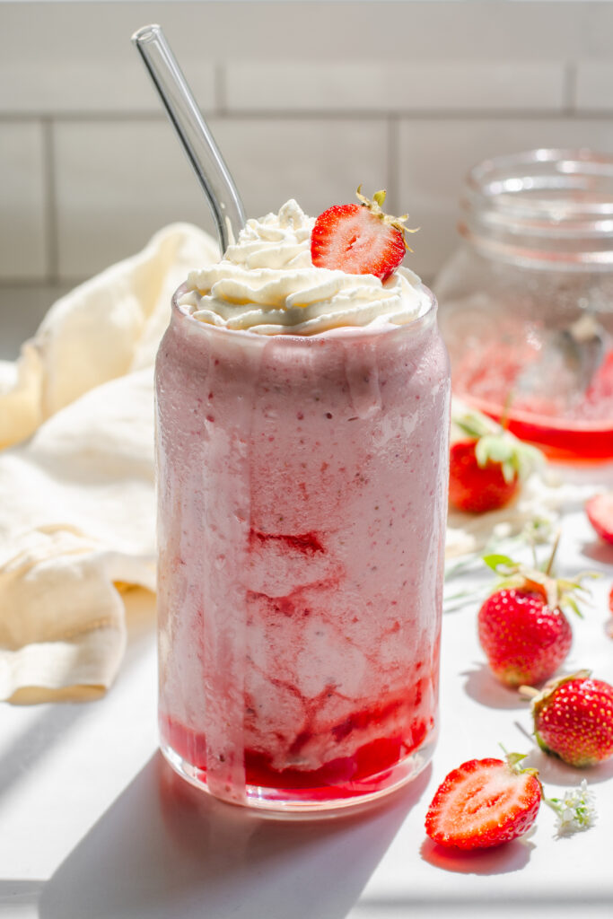 A strawberry milkshake made without ice cream on a white countertop with fresh strawberries to the side.