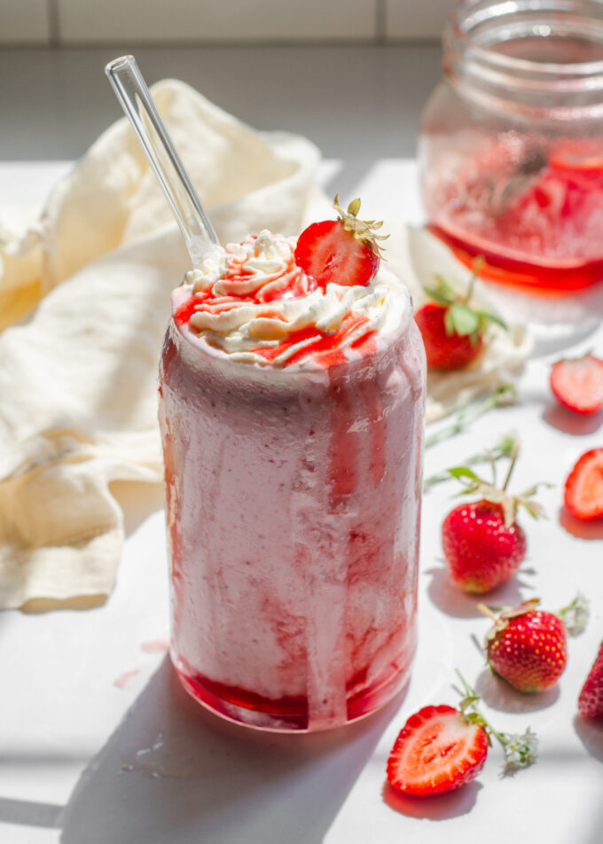 A strawberry milkshake made without ice cream on a white countertop with fresh strawberries to the side.