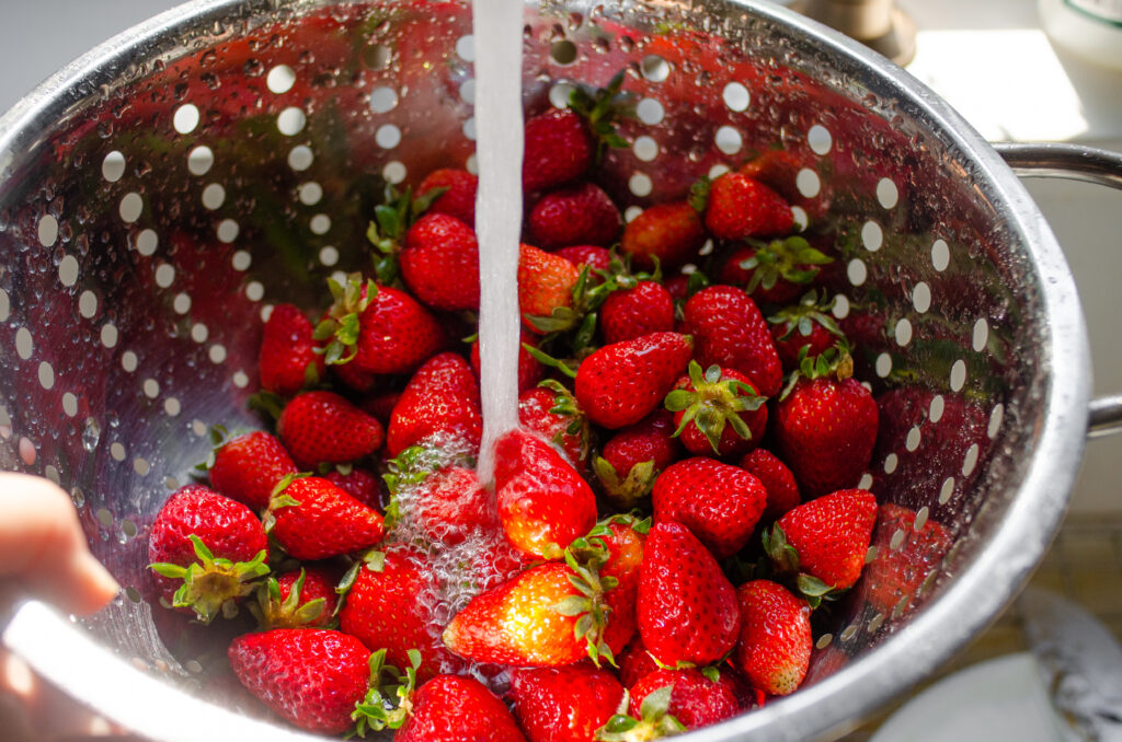 Washing strawberries in a stainless steel colander over the sink.