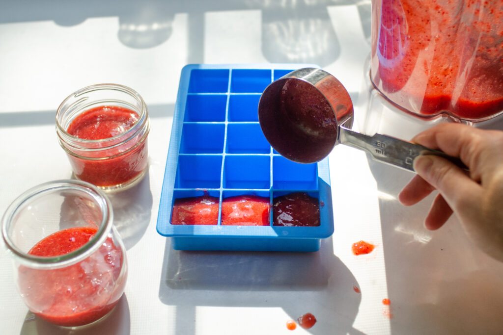 Pouring the strawberry puree into little jars and a silicone ice cube tray.