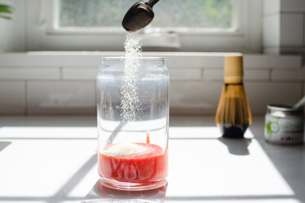 Adding the sugar to the strawberry puree in the glass.