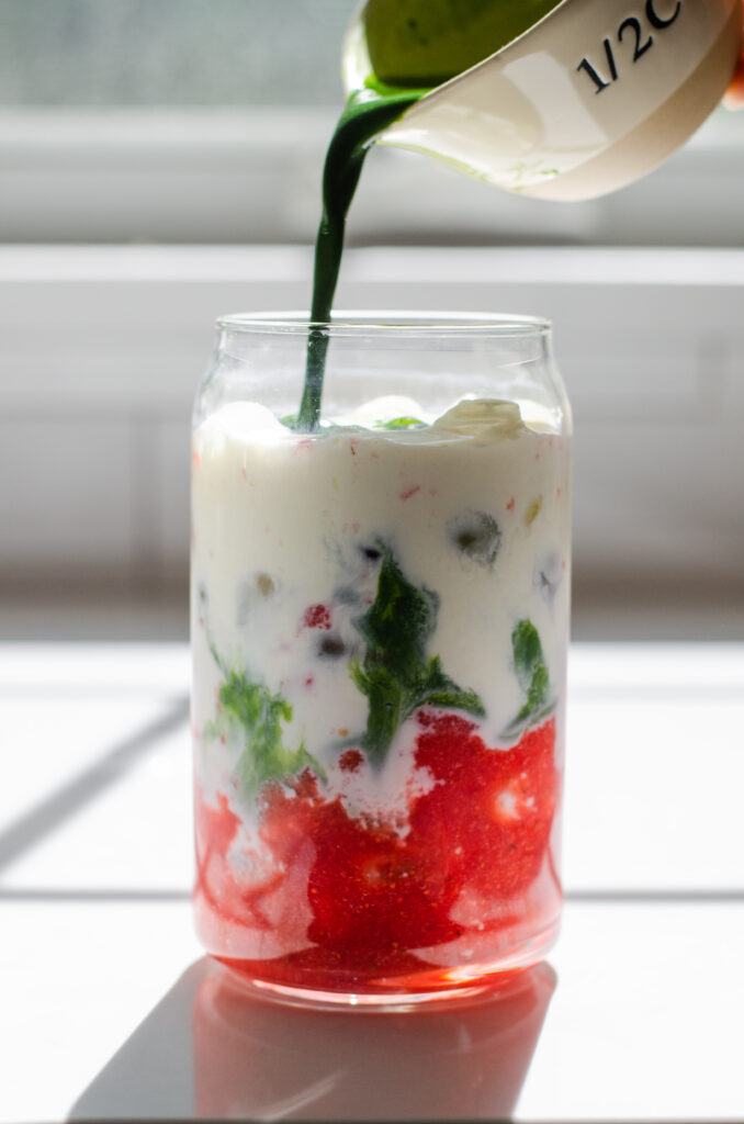 Pouring matching into a glass that has strawberry puree, ice and milk already in it to make a strawberry matcha latte.