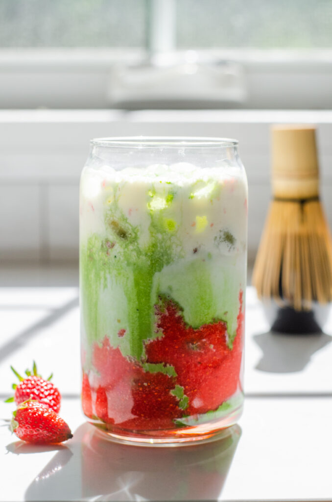 Pouring matching into a glass that has strawberry puree, ice and milk already in it to make a strawberry matcha latte.