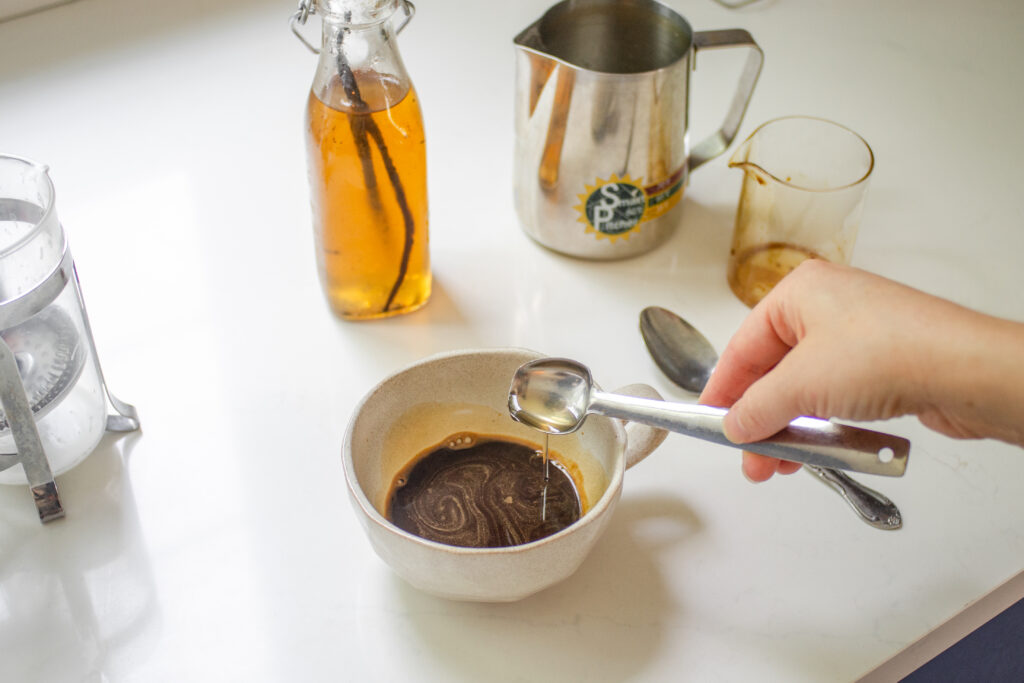 Adding vanilla syrup to coffee in a mug.