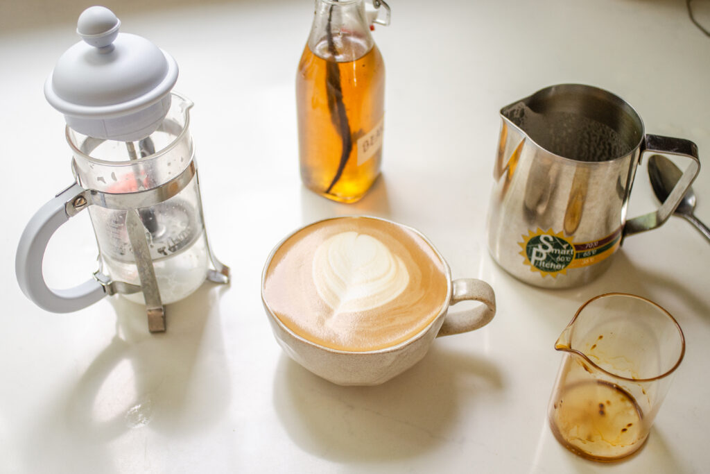 A mug filled with a copycat Starbucks latte with vanilla syrup and a French press in the background.