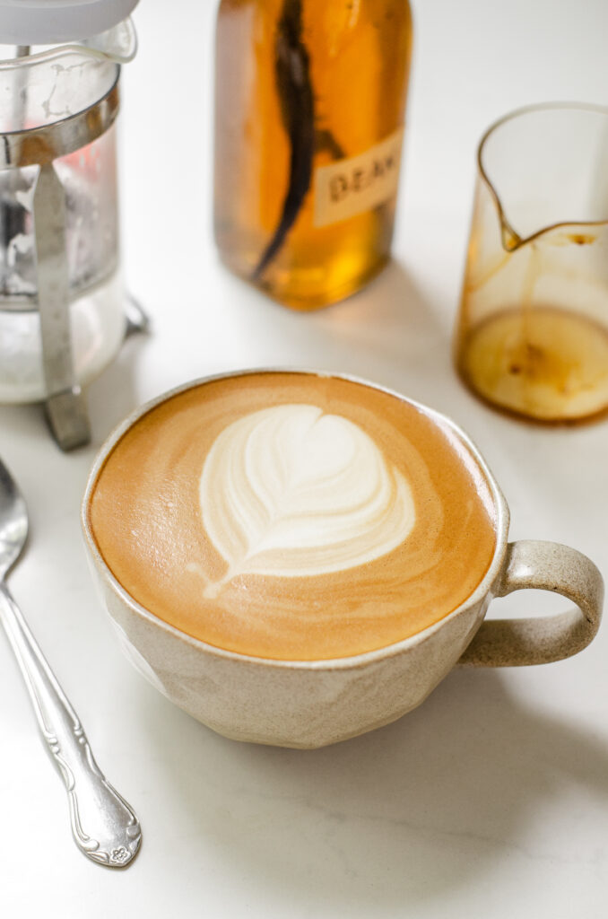 A mug filled with a copycat Starbucks latte with vanilla syrup and a French press in the background.