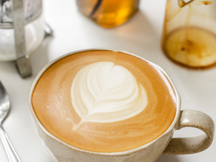 A mug filled with a copycat Starbucks latte with vanilla syrup and a French press in the background.