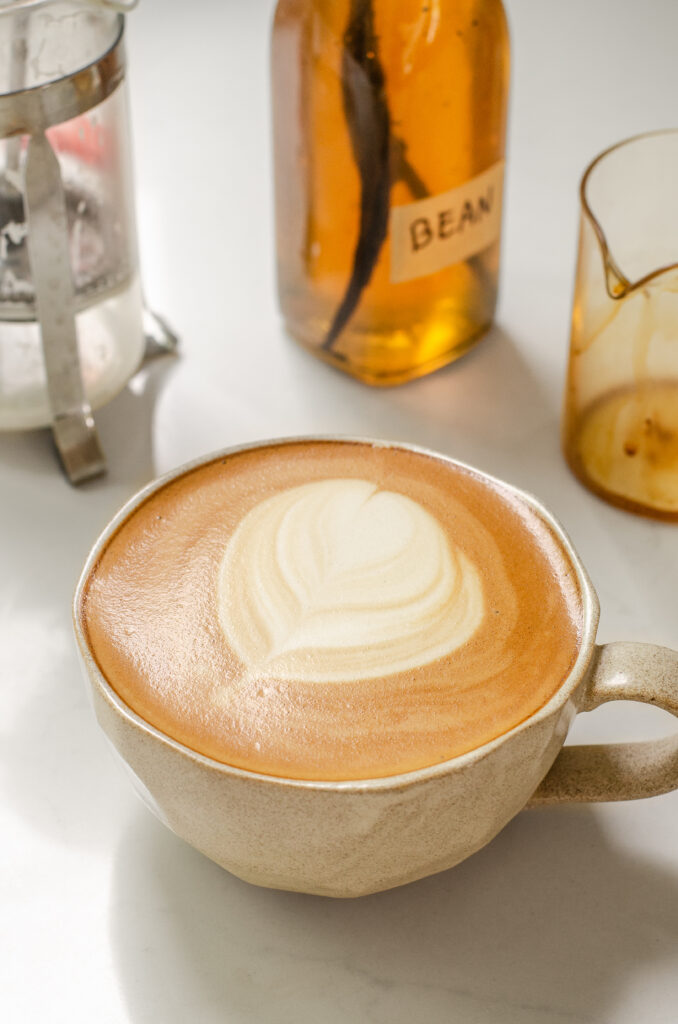 A mug filled with a copycat Starbucks latte with vanilla syrup and a French press in the background.