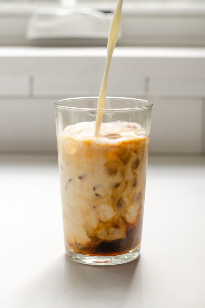 A homemade iced Starbucks latte in a 12 ounce glass with milk being poured into the glass.