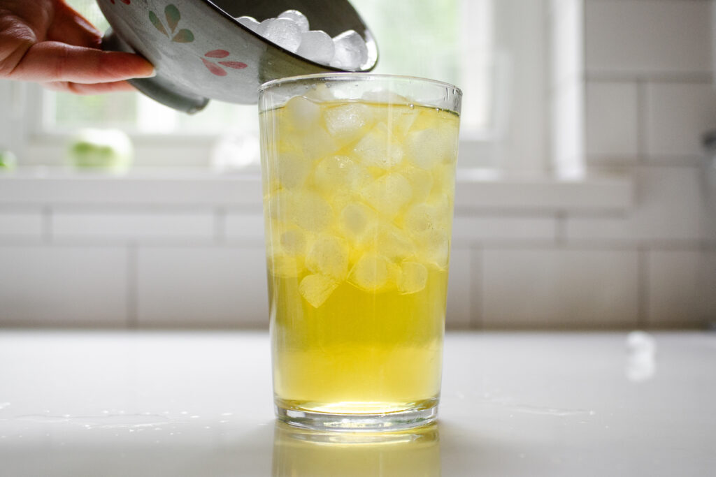 Pouring ice over the hot green tea to fill the glass.