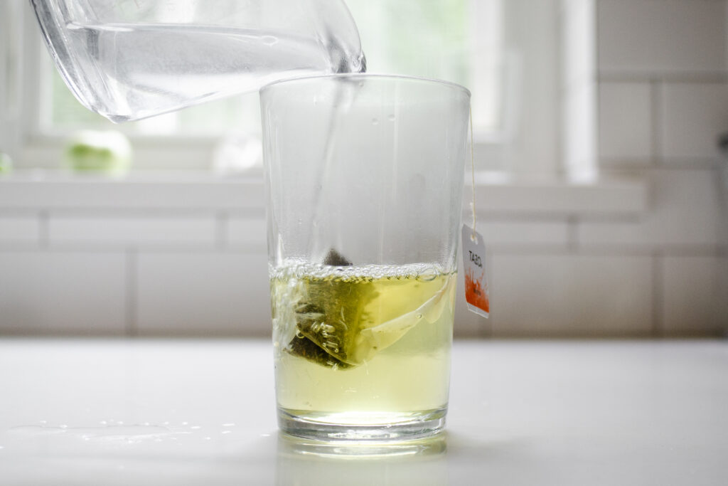 Pouring boil water on top of the tea bag in the glass.