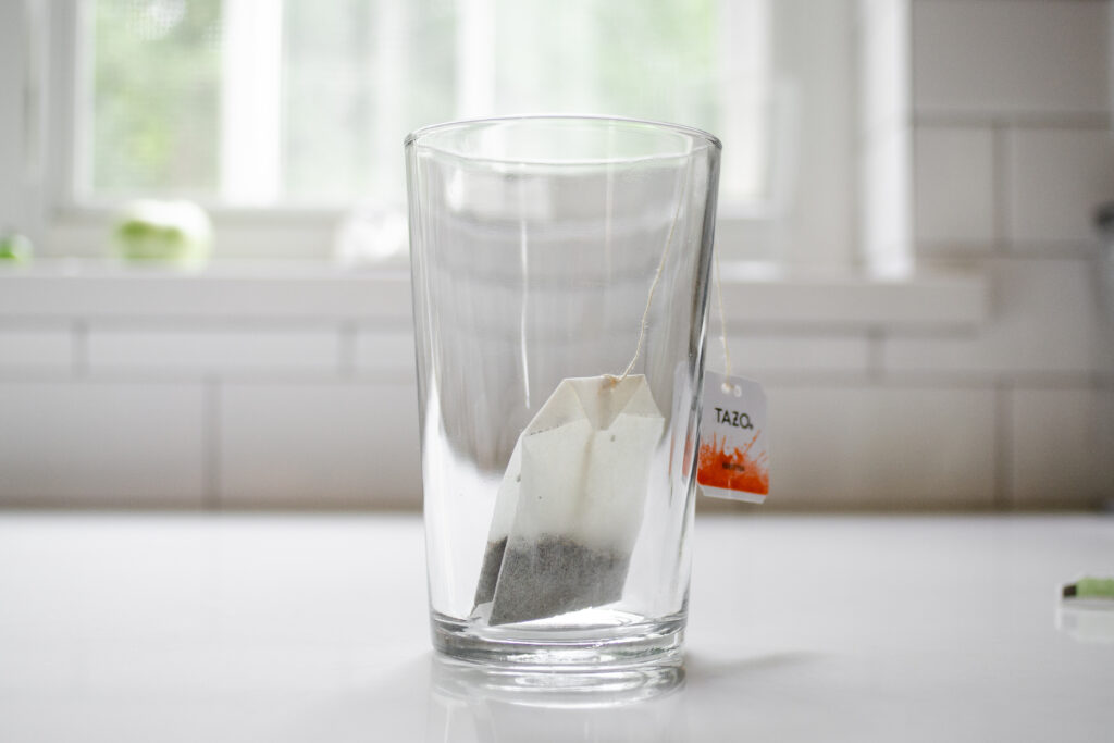 A green tea bag in a 12 ounce glass on a white countertop.