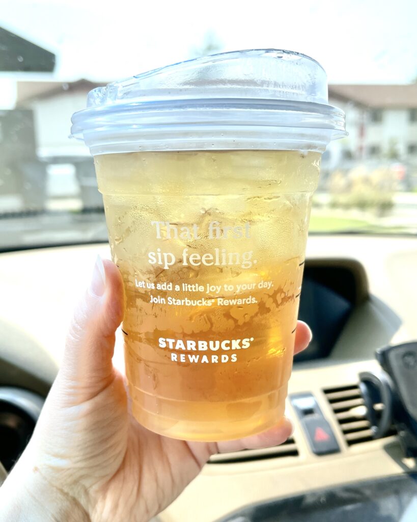 A hand holding a Starbucks cup of iced green tea while sitting in a car.