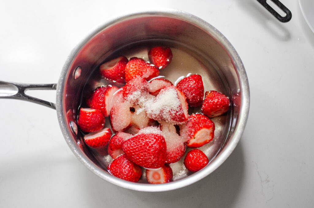 All of the ingredients needed to make strawberry syrup in a small saucepan.