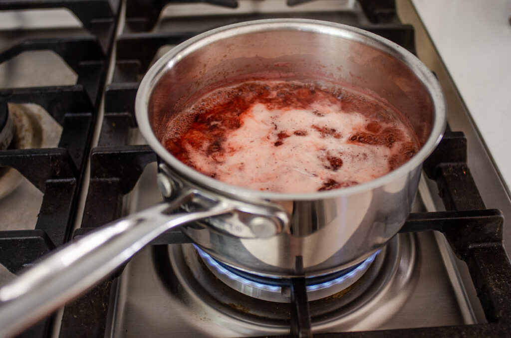 The simmered strawberry syrup in a small pan over the stove.