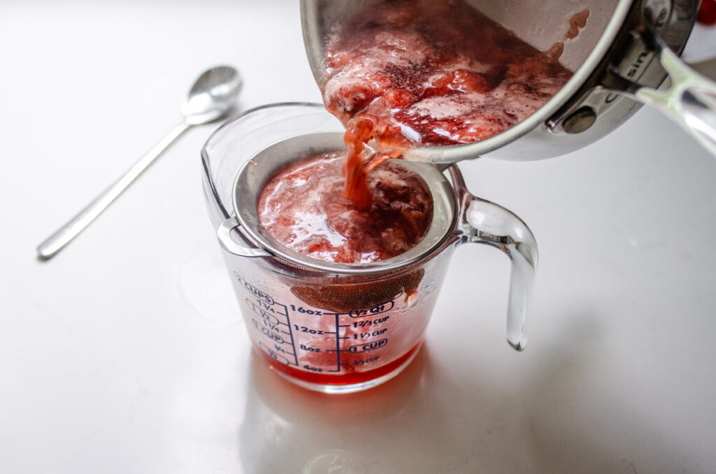 Pouring the cooked strawberry syrup through a fine mesh sieve.