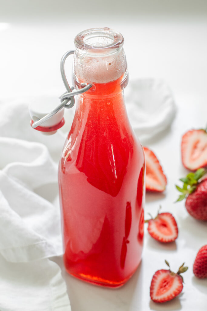 A bottle of homemade strawberry syrup intended to add to drinks.