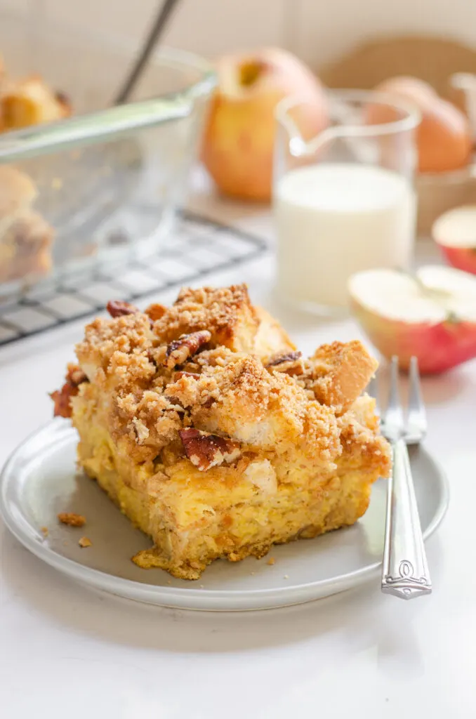 A slice of apple French toast casserole on a grey plate with apples in the background.
