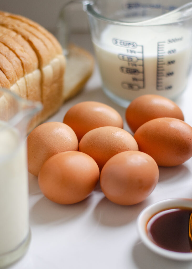 7 brown eggs on a white countertop with other ingredients around them.