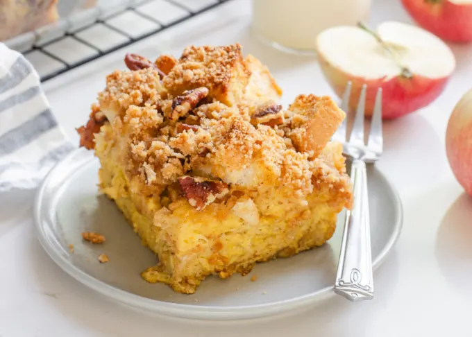 A slice of apple French toast casserole on a grey plate with apples in the background.