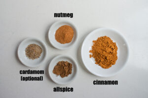 All of the ingredients needed to make apple pie spice in little white bowls.