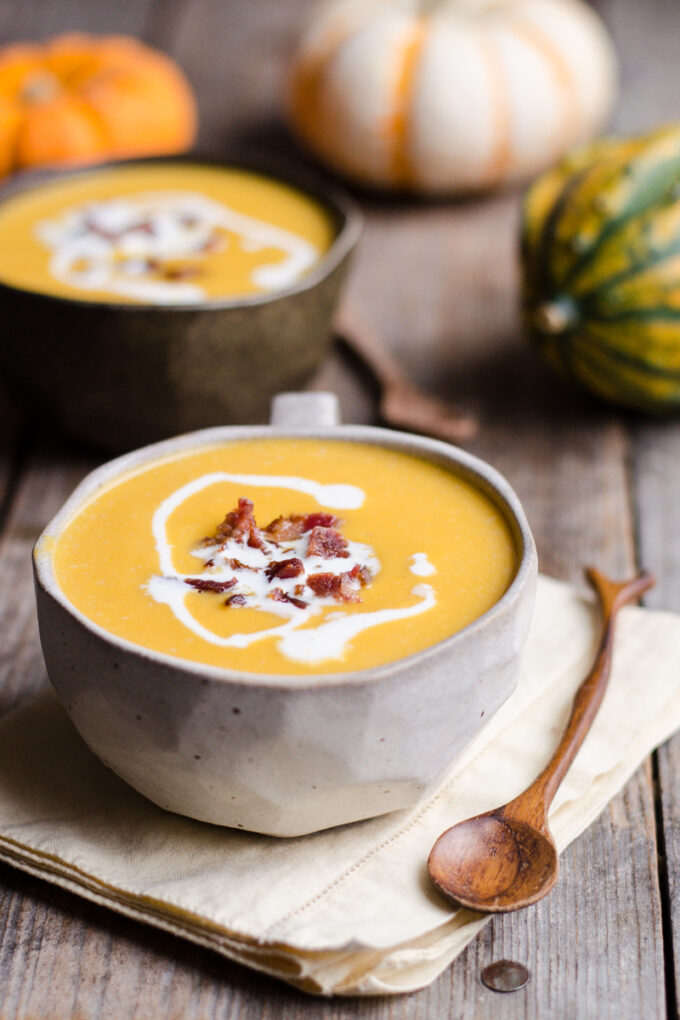 A bowl of roasted butternut squash bisque with mini pumpkins and squash around it.