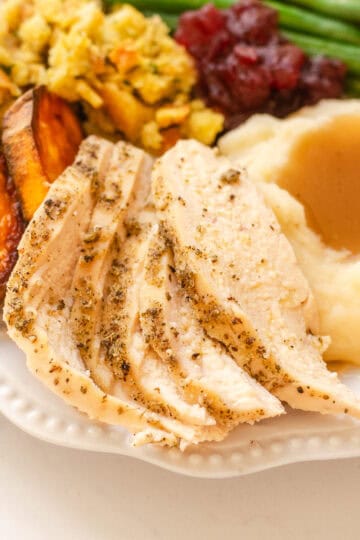 A plate of Thanksgiving dinner featuring green beans, mashed potatoes, gravy, stuffing, sweet potatoes, cranberry sauce, and chicken breast.