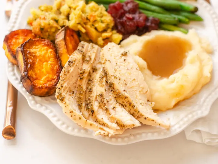 A plate of Thanksgiving dinner featuring green beans, mashed potatoes, gravy, stuffing, sweet potatoes, cranberry sauce, and chicken breast.
