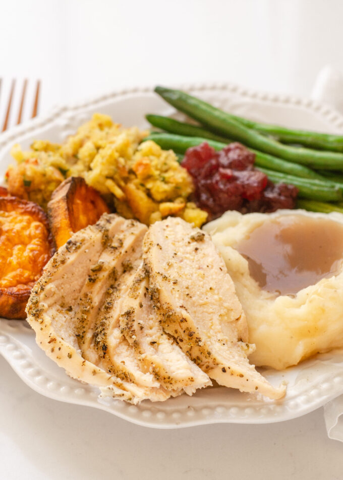 A plate of Thanksgiving dinner featuring green beans, mashed potatoes, gravy, stuffing, sweet potatoes, cranberry sauce, and chicken breast.