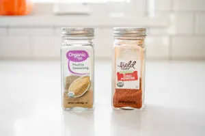A jar of poultry seasoning and chili powder on a white countertop.