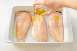 Pouring olive oil on boneless skinless chicken breasts in a baking dish.