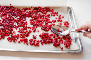 Placing pomegranate seeds on a parchment lined baking sheet to freeze.