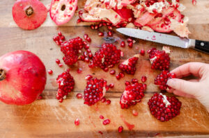 Sections of peeled pomegranate on a wooden cutting board.