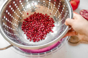 Lifting the colander and pomegranate seeds out of the bowl.