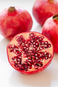 A pomegranate half on a white surface with whole pomegranates in the background.