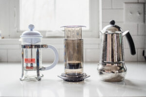 A French press, Aeropress, and Moka Pot on a white countertop.