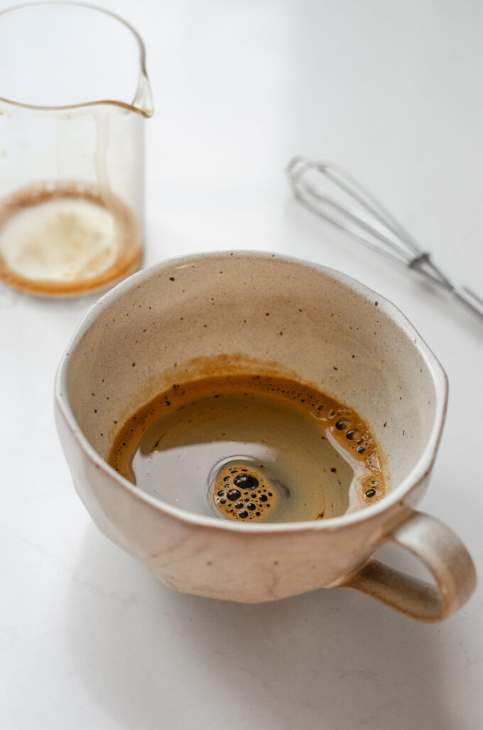 A shot of espresso made with instant coffee in a stoneware mug with a mini whisk and pitcher in the background.