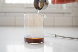 Pouring hot water over instant coffee in a mini glass pitcher.