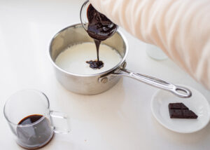 Pouring chocolate syrup into a pan of milk.