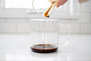 Pouring a shot of espresso into a clear glass mug.