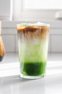 A 12 ounce glass of matcha coffee on a sunny white countertop with a white backsplash in the background