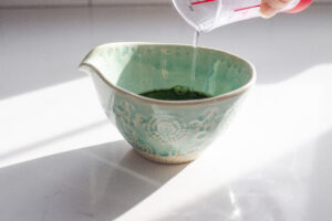 Pouring water on top of matcha and sugar in a small bowl.