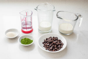 All of the ingredients needed to make an iced matcha coffee laid out on a white countertop.