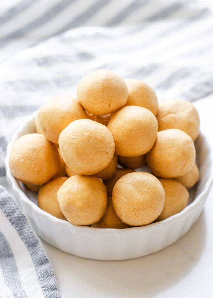 A ramekin filled with no bake peanut butter balls (without chocolate) with a striped linen napkin off to the side.