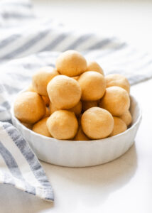 A ramekin filled with old fashioned peanut butter balls (without chocolate) with a striped linen napkin off to the side.