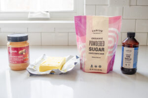 All of the ingredients needed to make no bake peanut butter balls on a white countertop with a window in the background. 